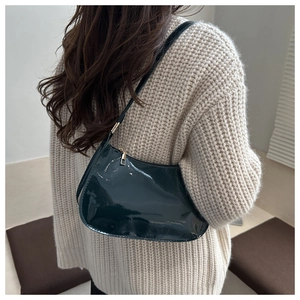 Deep green glossy patent leather hobo bag with gold hardware worn over a beige sweater