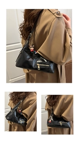 Detail of black glossy hobo bag with gold zippers and a red cartoon cow pendant charm