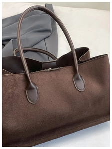 Detail of dark brown tote bag in textured suede material with slim leather handles