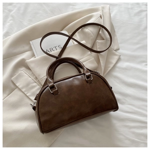 Close-up of brown PU leather bowling bag with silver hardware on beige blazer