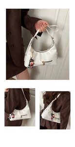Close-up of a white patent leather shoulder bag featuring a red bull charm and zipper details