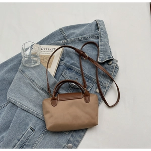 Detail of a beige nylon handbag with brown leather straps on a denim jacket background