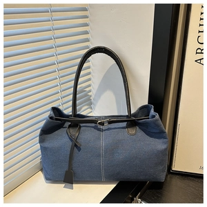 Detail of dark blue denim Boston bag featuring black leather handles and silver metal buckle