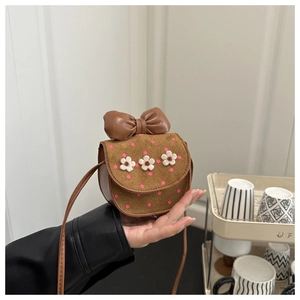 Détail d'un mini sac bandoulière marron avec nœud en cuir et broderies de fleurs 3D blanches