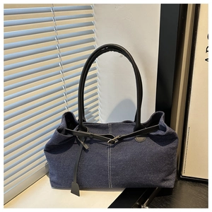 Detailed view of blue denim tote bag with black leather handles and silver buckle hardware