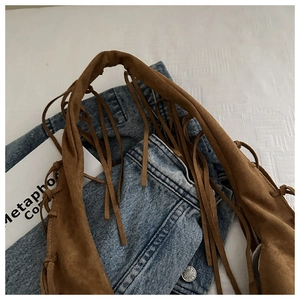 Détail macro du sac cabas en daim marron avec longues franges sur un jean bleu