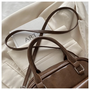 Close-up of textured dark brown PU leather Boston bag with cylindrical handles and metal hardware