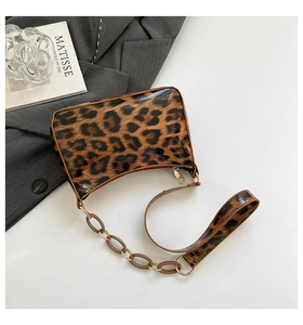 Detail of glossy leopard print shoulder bag with resin chain on a grey blazer backdrop