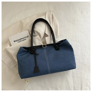 Detail of blue denim tote bag with contrast stitching and leather handles on white fabric