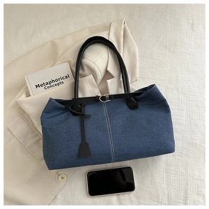Detail of blue denim tote bag with black leather handles on a minimalist lifestyle backdrop