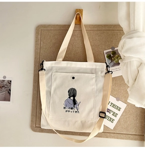 Detail of white canvas tote bag featuring minimalist girl illustration and front pocket