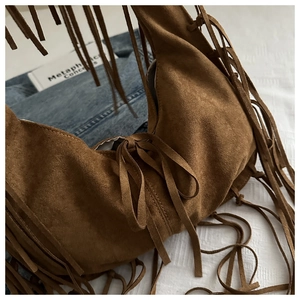 Détail du sac cabas en daim marron vintage avec de longues franges et des pompons bohèmes