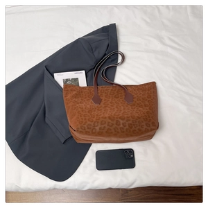 Detailed top view of leopard print tote bag with dark brown straps on a white textile