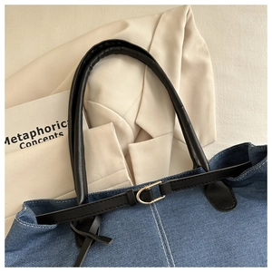 Detail of dark blue denim tote bag with white contrast stitching and golden hardware
