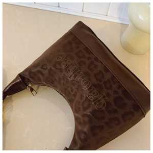 Detail of a dark brown leopard print crescent bag with gold zipper and stylish metal hardware