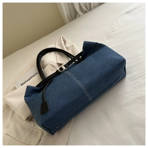 Detail of dark blue denim tote bag with white stitching and black leather handles