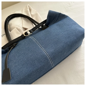 Close-up of deep blue denim tote with white stitching and black leather handles