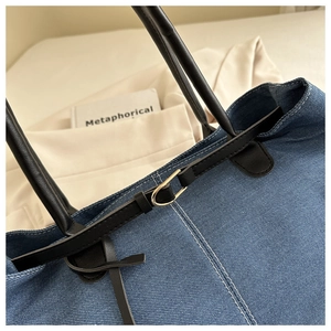 Detail of blue denim tote bag with black faux leather handles and golden metal buckle