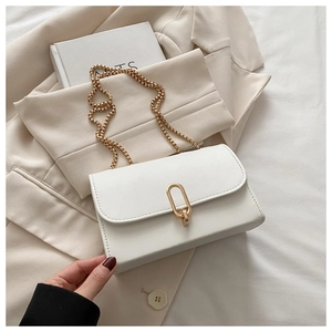 Close-up of minimalist white leather crossbody bag with gold oval buckle and chain strap