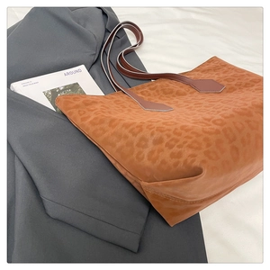 Detail of leopard print tote bag with brown straps placed on a stylish grey blazer