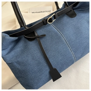 Detailed close-up of blue denim tote bag featuring black leather handles and stitching