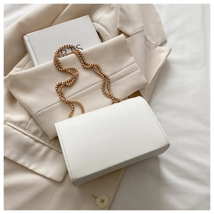 Close-up of ivory white rectangular handbag with gold chain strap and stitching detail