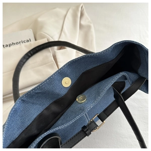 Detail of blue denim tote bag with magnetic gold buckle and black leather strap handles