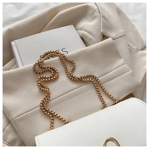 Close-up of white leather crossbody bag with golden chain strap on a beige blazer
