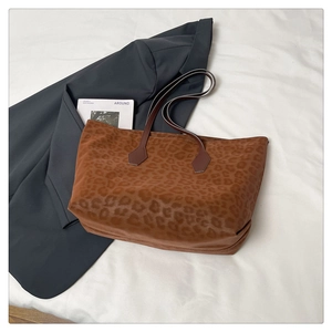 Close-up of leopard print tote bag with brown handles next to a blazer and lifestyle book