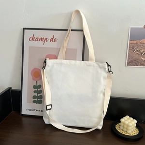 Detail of white canvas tote bag with adjustable shoulder strap on a minimalist desk