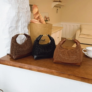 Three leopard print suede hobo bags in dark brown, black, and light tan on a wooden table