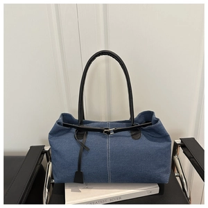 Blue denim tote bag with black handles and white stitching detail on a leather seat