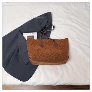 Macro shot of large leopard print tote bag on white cloth with magazine and grey blazer