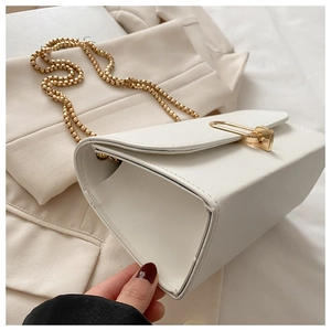 Detailed view of a white minimalist bag with a gold spherical chain on a blazer