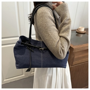Dettaglio della borsa tote in denim blu con tracolla nera indossata da una modella