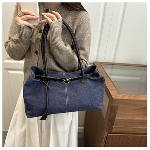 Detail of blue denim tote bag featuring black leather straps and buckle on the shoulder