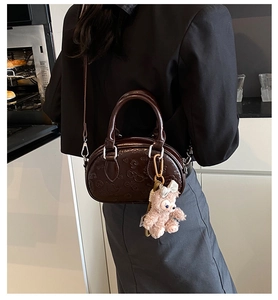 Sac Boston marron foncé avec motifs en relief et breloque peluche rose sur modèle