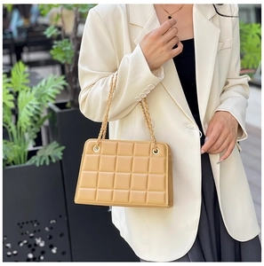 Detail of light brown quilted crossbody bag with golden chain strap on white blazer