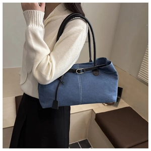Detail of blue denim tote bag featuring black leather straps and white contrast stitching
