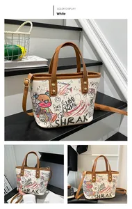 Détail du cabas graffiti blanc avec imprimés cartoon, anses en cuir marron et détails dorés