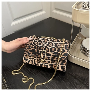 Detail of leopard print crossbody bag with gold chain strap and metal clasp on wood surface
