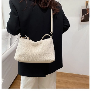 Modellansicht der cremefarbenen Plüsch-Eimertasche mit Lederriemen auf schwarzem Blazer