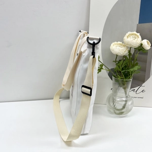 Detail of white canvas shoulder bag featuring black metal hooks and adjustable strap