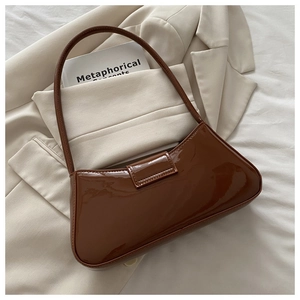 Close-up of glossy brown patent leather shoulder bag on a stylish beige blazer background