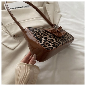 Detail of leopard print fabric textures and sleek brown leather bow on an underarm bag