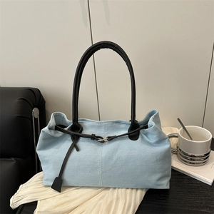 Light blue denim tote bag with black leather straps and decorative buckle in a soft setting