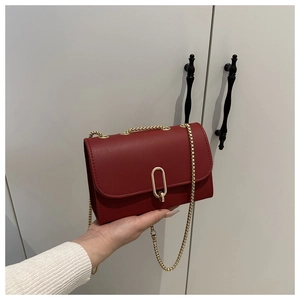 Detail of red PU leather flap bag featuring elegant gold oval lock and thin chain strap