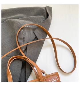 Gros plan sur un sac bandoulière en cuir marron avec texte graffiti sur blazer gris