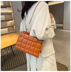 Brown quilted chain bag shown on model's shoulder with elegant gold metal strap detail