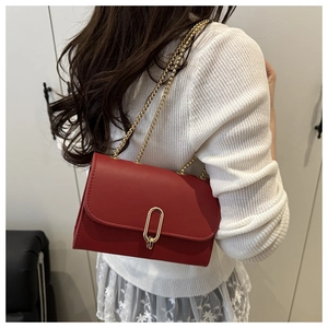 Red textured leather flap bag with gold oval clasp and chain strap on a white sweater